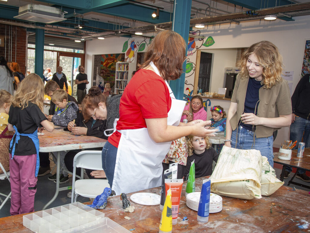 A studio volunteer offering support to a community member, assisting with creative skills.